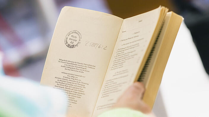 Aufgeschlagenes Buch mit Stempel "Pflichtexemplar" von Händen gehalten