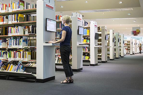 Frau in der Lesehalle der AGB steht an Katalog PC und recherchiert