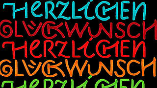 Bunte Schrift "Herzlichen Glückwunsch" auf schwarzem Hintergrund.