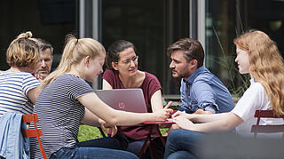 People sit together in the courtyard at a table with a laptop and talk to each other