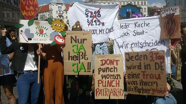 Ein Foto von einer Demo mit unterschiedlichen Transparenten und Plakaten