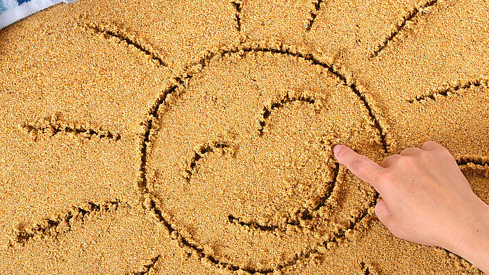 Hand malt Sonne im Sand