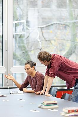 Zwei Männer unterhalten sich angeregt vor Laptop der vor Ihnen auf einem Tisch steht