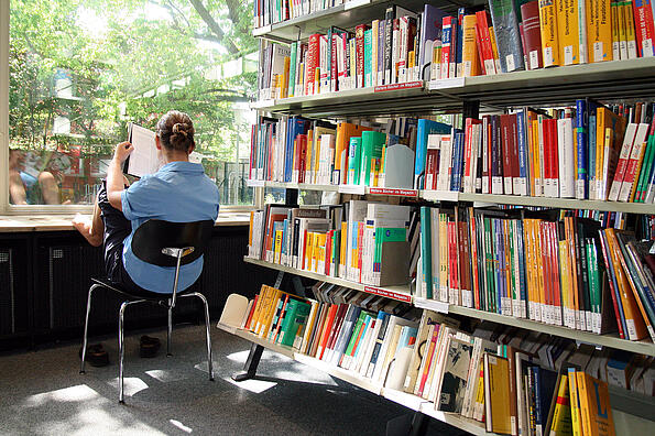 Nutzer sitz in der Bibliothek am Fenster und liest in einem Buch