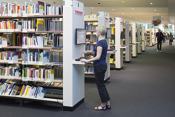 Frau steht an PC Bildschirm in der Lesehalle der AGB