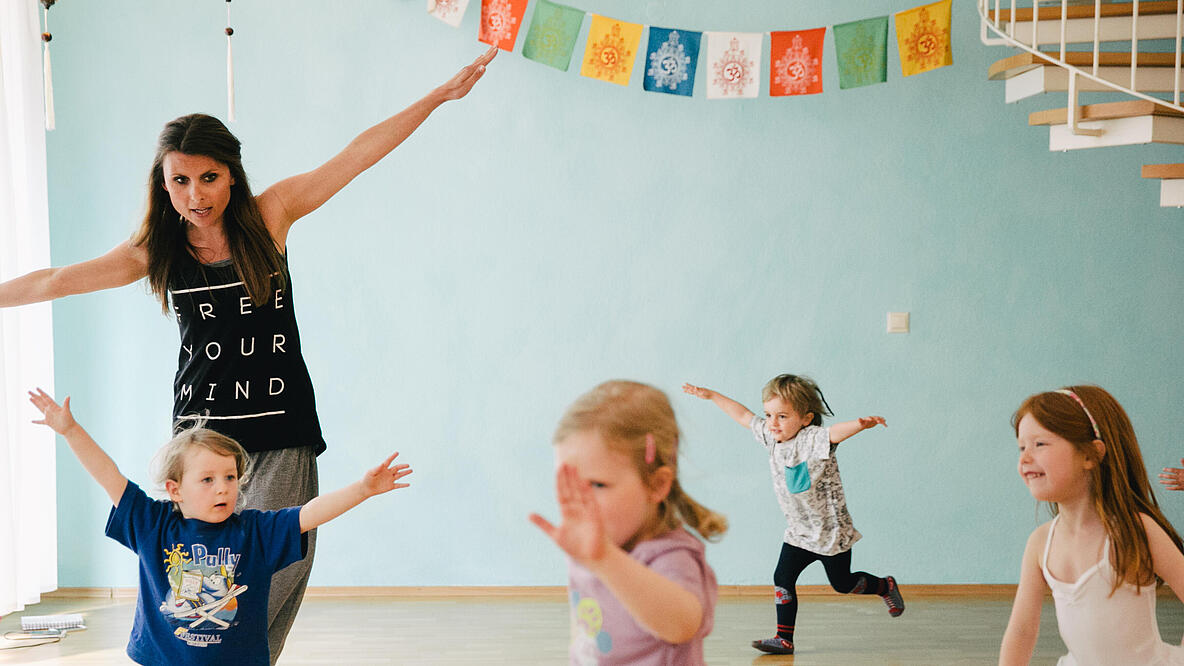 vier Kinder tanzen im Raum verstreut in Begleitung einer Frau durch den Raum