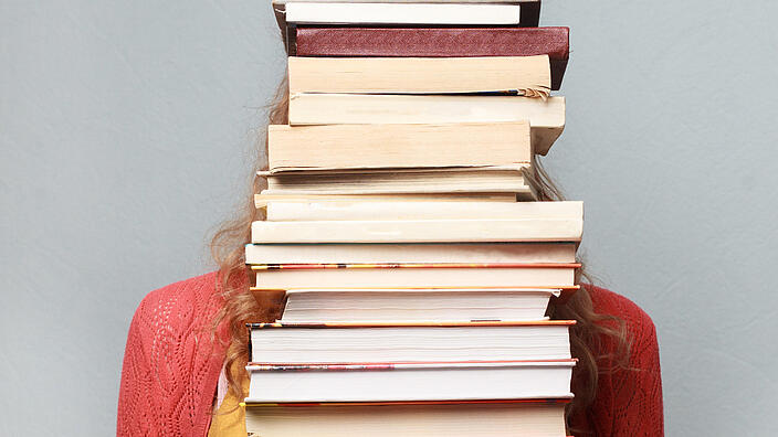 Foto von Frau mit Bücherstapel vor dem Kopf