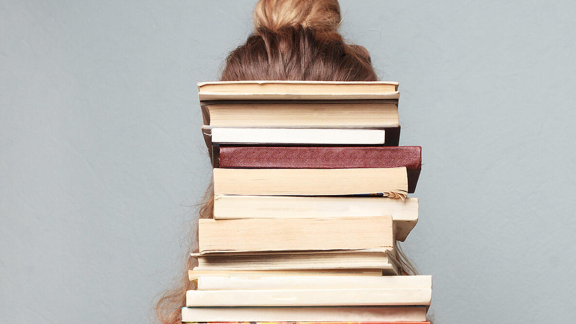 Foto von Frau mit Bücherstapel vor dem Kopf