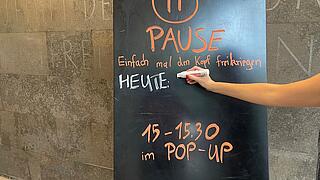 Foto einer beschrifteten schwarzen Tafel, auf der eine Person etwas Neues hinzu schreibt