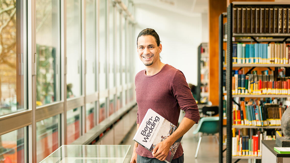 Junger Mann im Lesesaal der Berlin-Sammlungen mit Buch "Berlin-Wedding" in der Hand