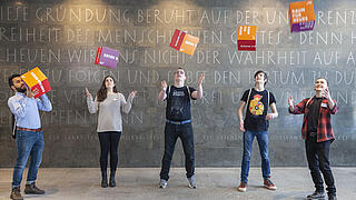 Auszubildende im Foyer der AGB werfen Pappwürfel mit der Aufschrift Raum für neues in die Luft